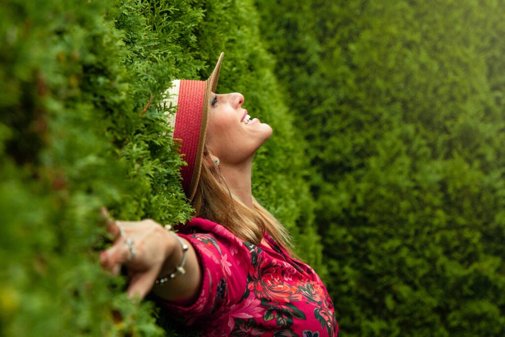 woman smiling happy against a green hedge wall