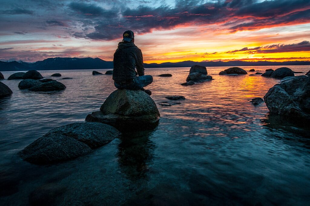 man meditating sitting on a rock staring at the sea during the sunset