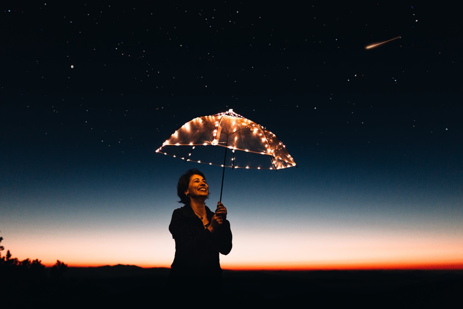 happy woman smiling holding an umbrella with lights under a starry night