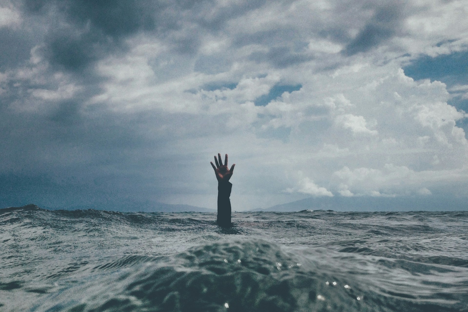 a hand reaching out from the middle of the ocean up to the sky seeking for help