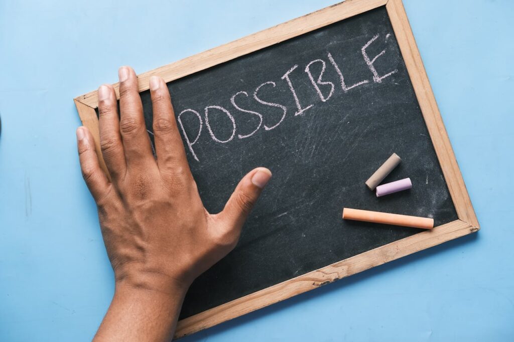 a hand covering "im" and showing "possible" on a small chalkboard